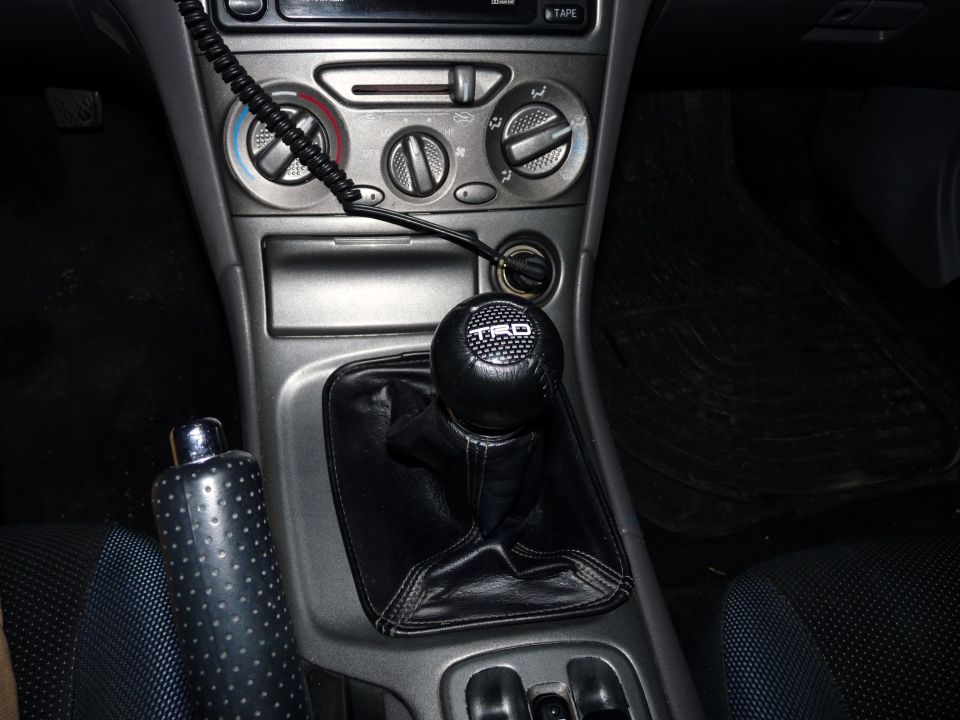 Car interior showing a TRD shift knob, center console with climate controls, and a perforated handbrake grip