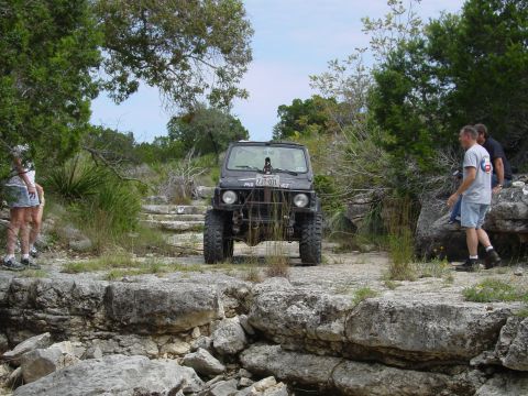 1973 Ford Bronco - A group of people stand near a modified off-road vehicle on a rocky, natural trail.