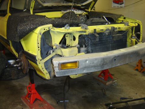 1979 Ford Mustang - The front end of a yellow vehicle is disassembled and supported by jack stands in a garage.