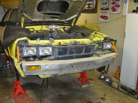 1979 Ford Mustang - Front view of a yellow 1979 Ford Mustang undergoing repairs in a garage, with the hood open and bumper removed.