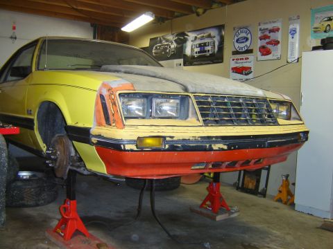1979 Ford Mustang - Front view of a yellow 1979 Ford Mustang with its front end raised on jack stands in a garage.