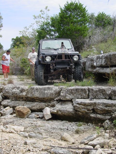 1973 Ford Bronco - A modified off-road vehicle navigates a rocky trail with two people nearby.