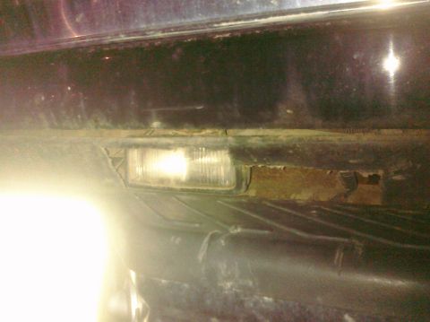 1995 Ford Bronco - The front bumper area of a vehicle shows a fog light and signs of wear and tear.