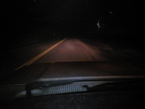1989 Ford Bronco - View from inside a vehicle driving on a dark road at night with double yellow lines.