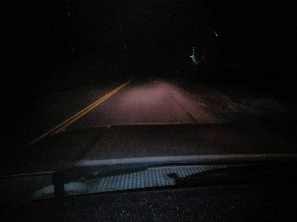 Dashboard view of a road at night with headlights illuminating the fog