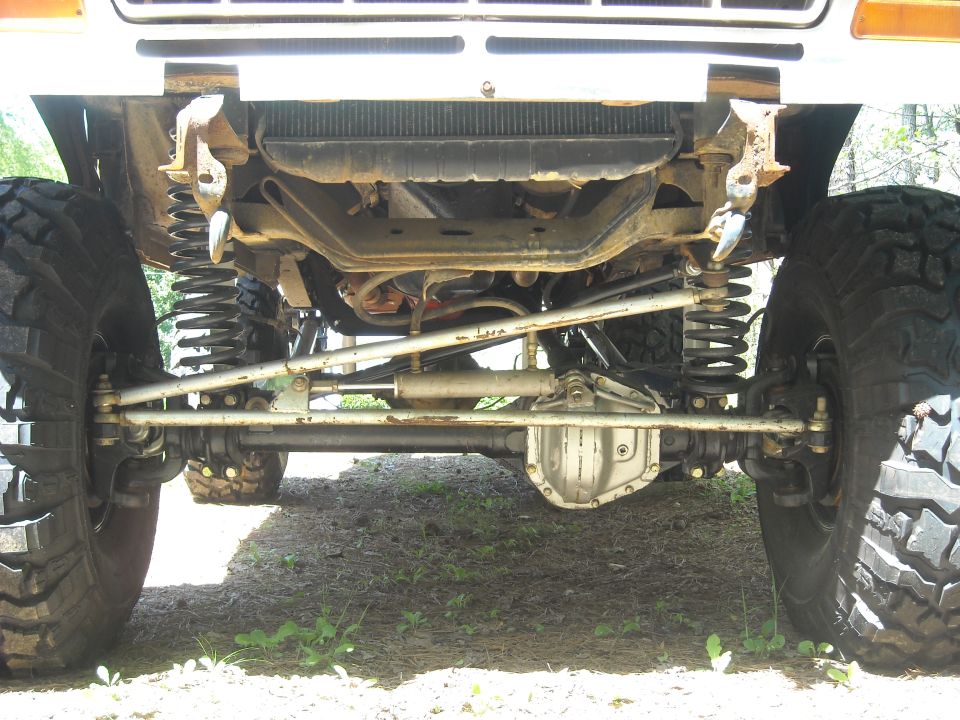 Underside view of a truck's front axle, suspension, and large tires