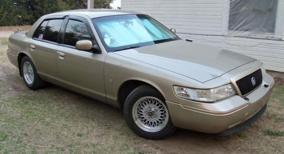 Gold Mercury Grand Marquis sedan on mesh wheels parked beside a white house