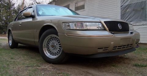 2000 Mercury Grand Marquis - The front passenger side of a gold Mercury Grand Marquis is shown, aftermarket BBS-style wheels and a black grille.