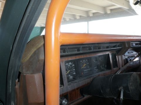 1982 Ford Bronco - The interior of a vehicle shows an orange roll cage, dashboard gauges, and wood-grain trim.