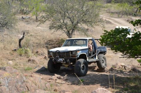 1986 Ford Bronco - Off-road Bronco navigates a rocky path, with a second vehicle in the distance.
