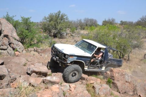 1986 Ford Bronco - This modified off-road vehicle navigates a challenging rocky trail under a clear blue sky.