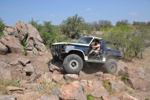 1986 Ford Bronco - A modified Ford Bronco navigates a rocky, off-road trail with a driver behind the wheel.