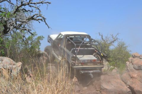 1986 Ford Bronco - This heavily modified off-road vehicle navigates a steep, rocky incline under a clear blue sky.