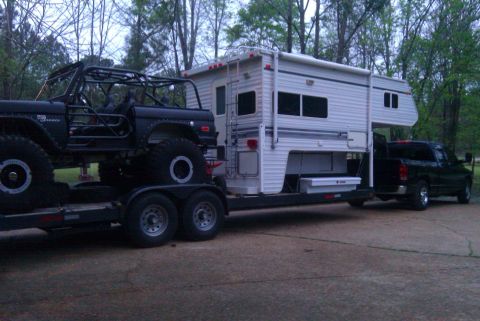 1967 Ford Mustang - A heavily modified black 1966 Ford Bronco is transported on a trailer, accompanied by a camper and a pickup truck.
