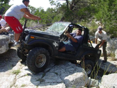 1973 Ford Bronco - A group of people assist an off-road vehicle as it navigates a challenging rocky path.