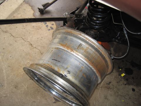 1979 Ford Bronco - A close-up view of a rusty wheel and suspension parts on a concrete surface.