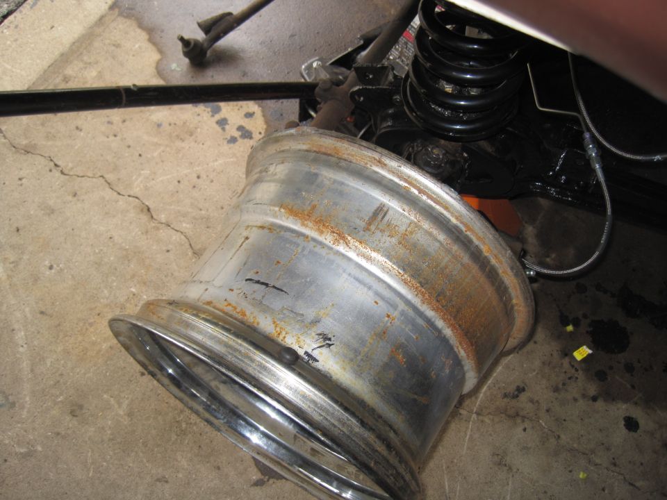 Rusted aluminum wheel and black coil spring on concrete floor