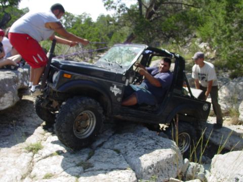 1973 Ford Bronco - People assist an off-road vehicle navigating a rocky terrain.