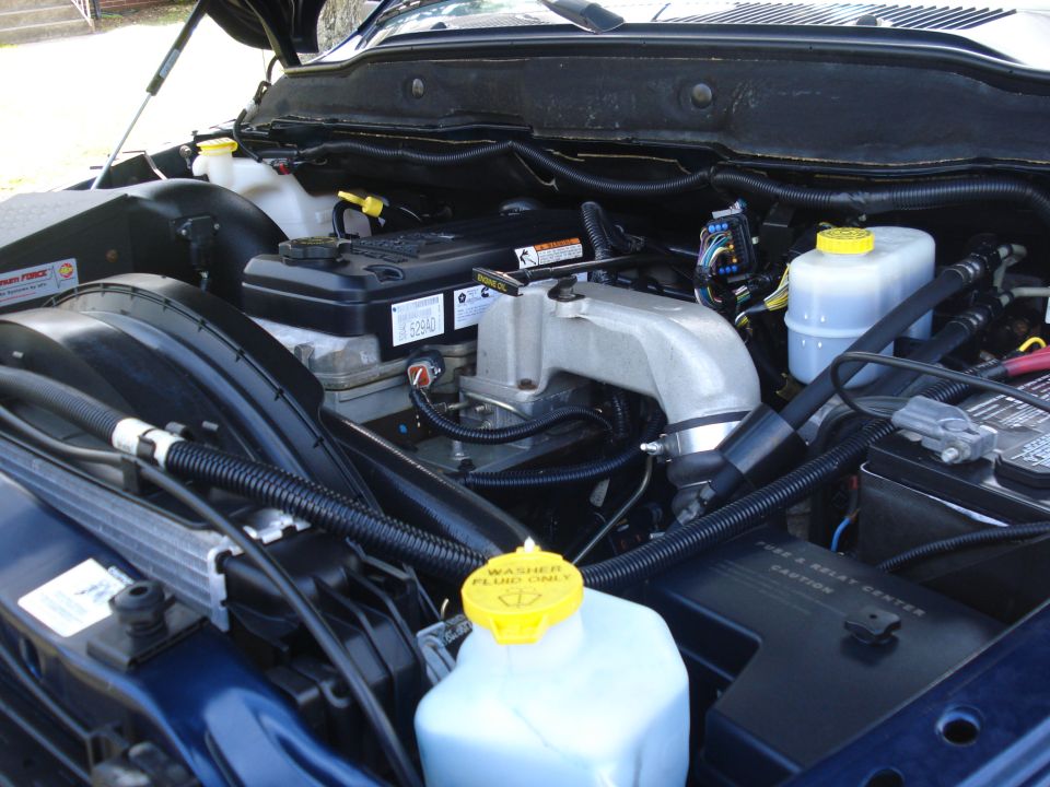Engine bay of a blue 2005 Dodge 2500, showing the Cummins diesel engine, washer fluid reservoir, and battery