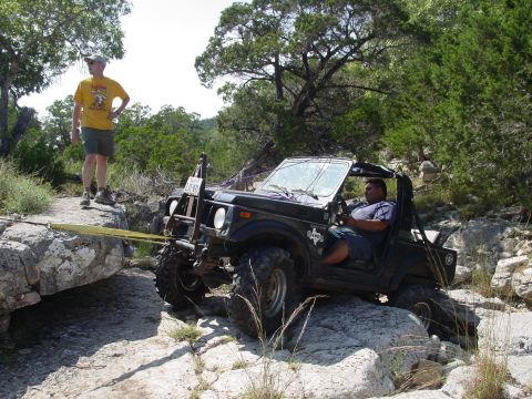 1973 Ford Bronco - An off-road vehicle navigates a challenging rocky path, with a tow strap assisting its progress.