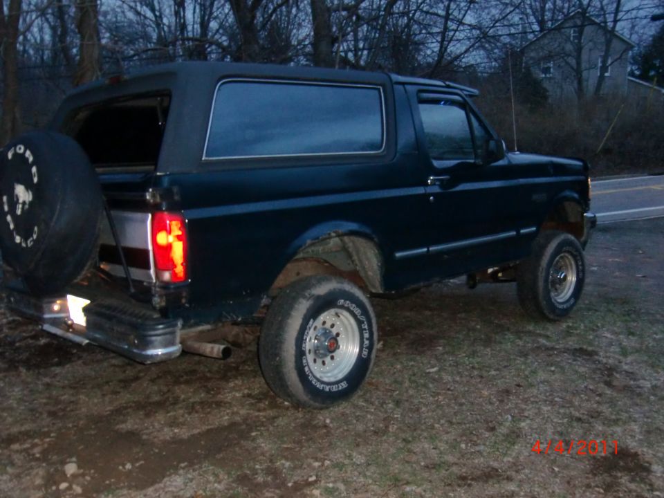 Dark blue Ford Bronco with a soft top, spare tire on the rear, and aftermarket wheels