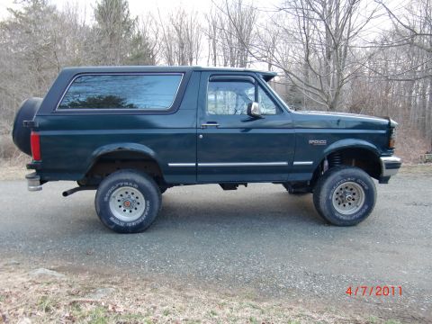 1993 Ford Bronco - A dark green 1993 Ford Bronco is shown from the side, lifted with large tires and a spare tire mounted on the back.