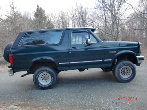 1993 Ford Bronco - This lifted 1993 Ford Bronco is shown from the side, its dark green paint and rear-mounted spare tire.