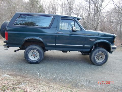 1993 Ford Bronco - Side view of a dark green 1993 Ford Bronco, showing its lifted suspension and spare tire.