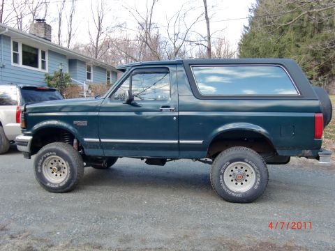 1993 Ford Bronco - A lifted 1993 Ford Bronco is shown from the side, parked in a driveway next to another vehicle.