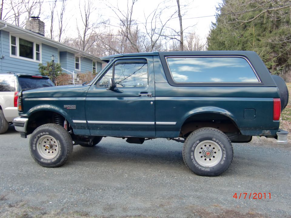 Green Ford Bronco parked outside a house. Another SUV is parked next to it