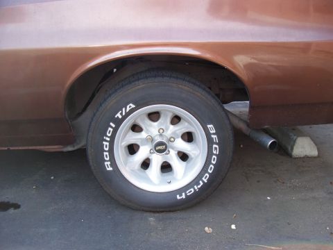 1972 Ford Ranchero - The rear wheel and fender of a brown vehicle are shown, with a visible exhaust pipe resting on blocks.