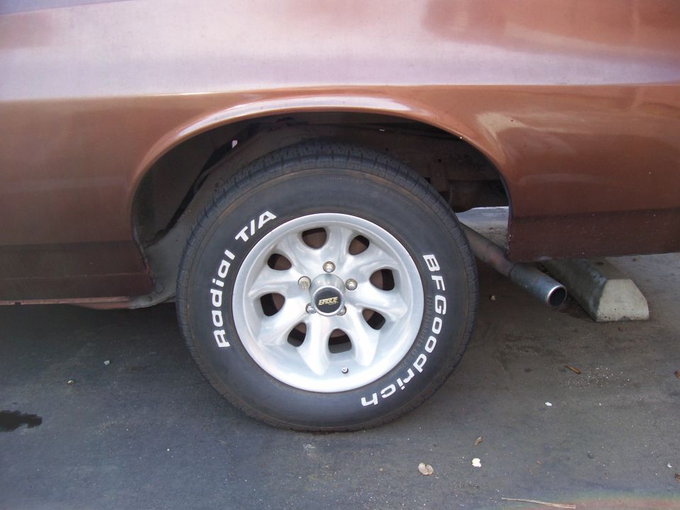 Close-up of a car's rear wheel with BFGoodrich Radial T/A tires and aftermarket wheels. Exhaust pipe visible