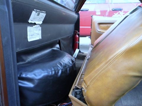 1972 Ford Ranchero - The interior of a vehicle is shown, with a spare tire cover and a fire extinguisher visible, alongside tan seats and a red vehicle in the b…