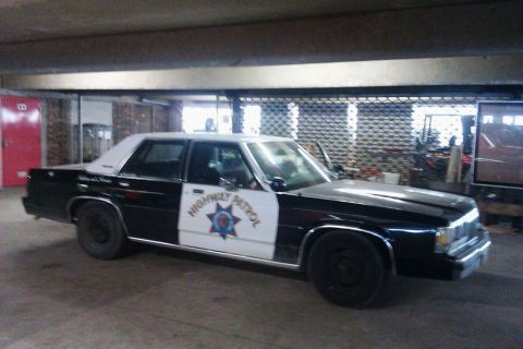 1991 Ford LTD Crown Victoria - Black-and-white Ford LTD Crown Victoria patrol sedan parked under a concrete garage structure, shown from the front three-quarter with "HIG…