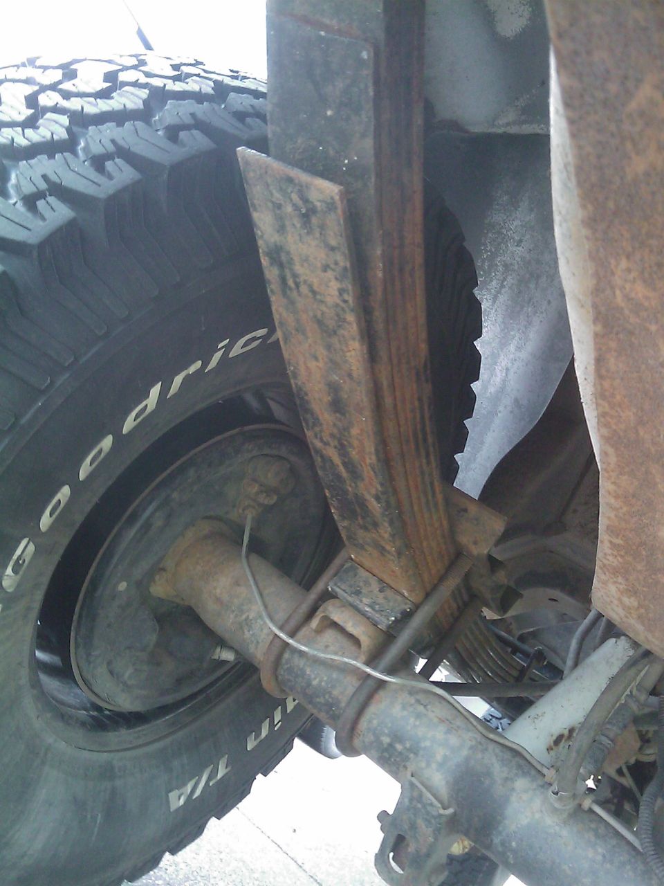 Close-up of rusty rear leaf spring pack, U-bolts and shock beside a BFGoodrich A/T tire