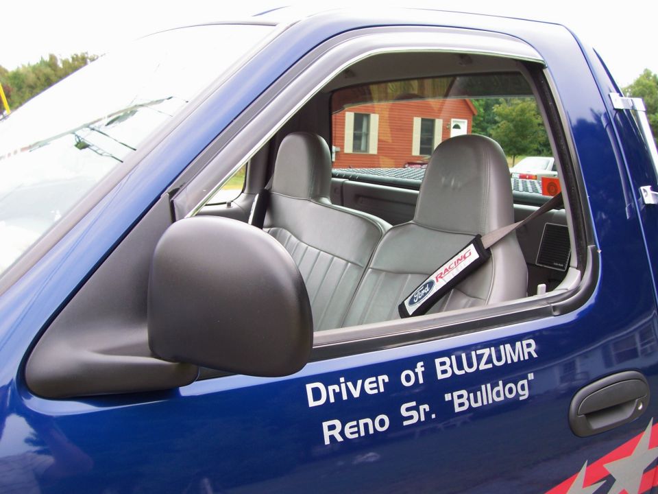 Blue Ford truck interior with gray seats and a Ford Racing seatbelt cover. Text on door reads 'Driver of BLUZUMR Reno Sr. "Bulldog"'