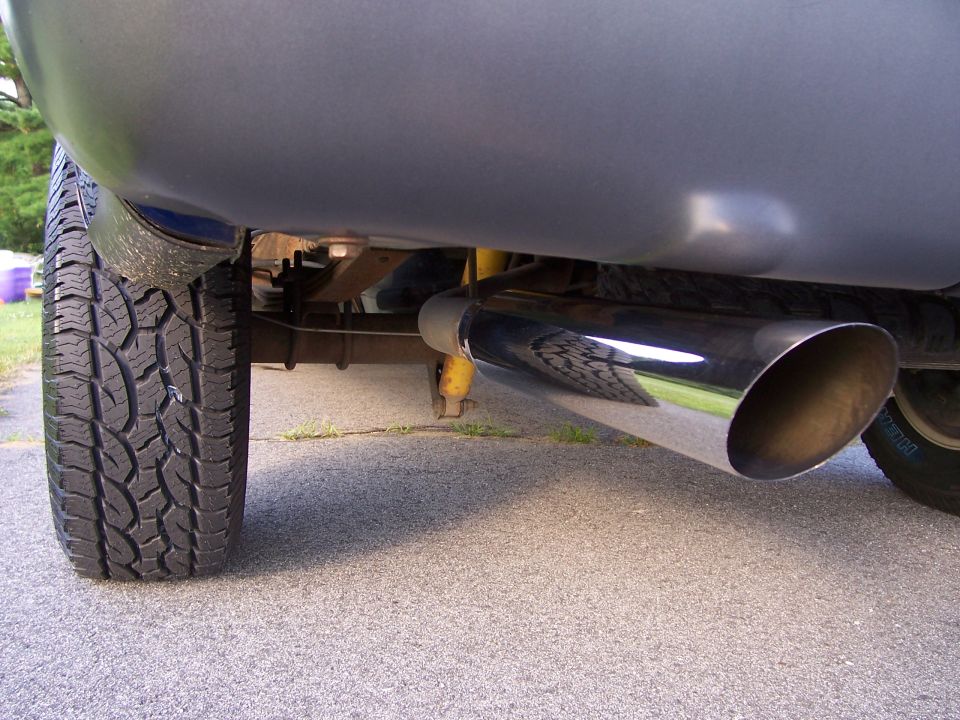 Underbody view of pickup rear tire and polished angled exhaust tip on driveway