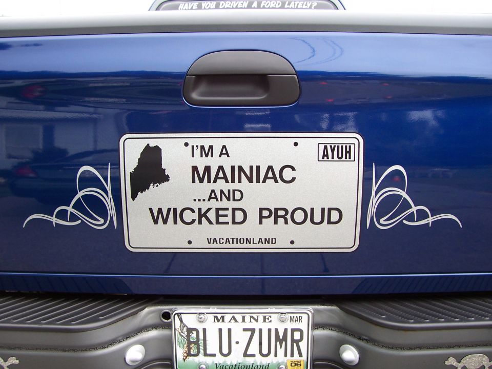 Blue pickup truck tailgate with a Maine license plate frame and a custom plate reading "I'M A MAINIAC ...AND WICKED PROUD"
