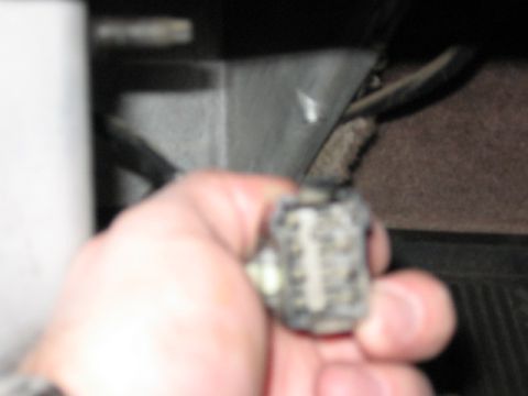 1995 Ford Bronco - A hand holds a small dark electrical connector plug with visible metal pins/terminals, photographed close up in a vehicle interior footwell…