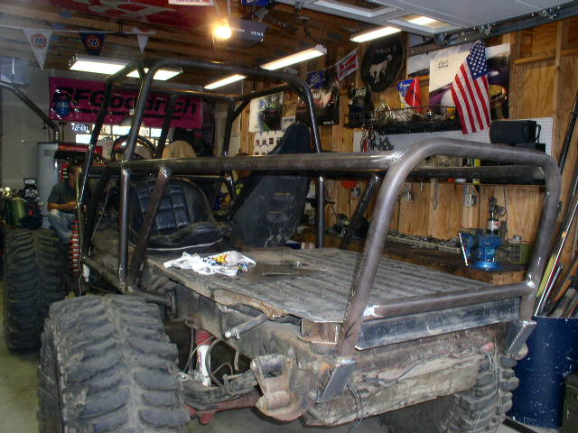 custom buggy frame with roll cage, large tires, and seats, in a garage