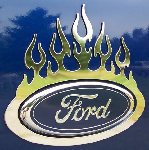 1998 Ford F-150 - A chrome Ford emblem is adorned with stylized flames, reflecting the sky and clouds.