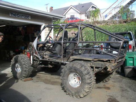 1979 Ford Bronco - A heavily modified off-road buggy with a custom roll cage sits outside a garage, with another vehicle visible in the background.