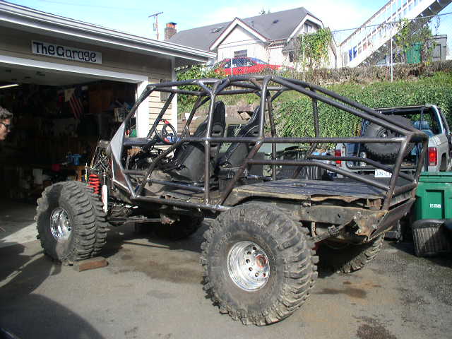 Bare tube-frame rock buggy with full roll cage and oversized mud tires parked in a driveway