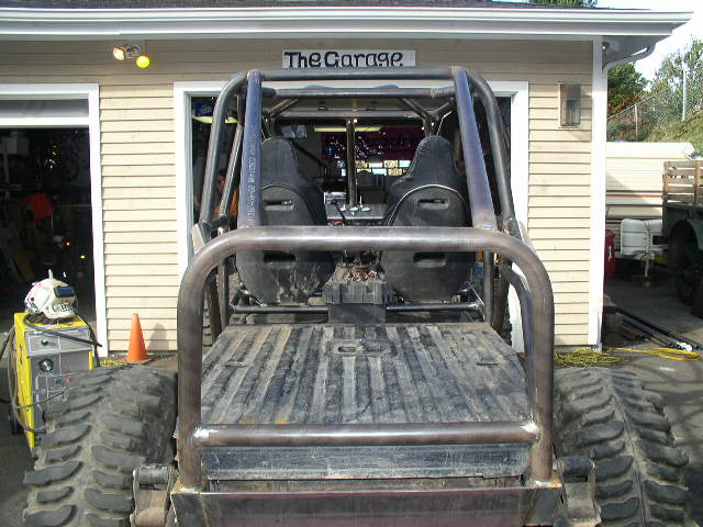 Rear view of bare-metal tube-frame buggy with two racing seats parked outside a garage