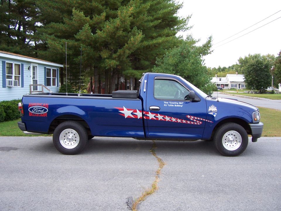 Dark blue Ford F-150 regular cab long bed with star graphics and bed toolbox, side view in driveway