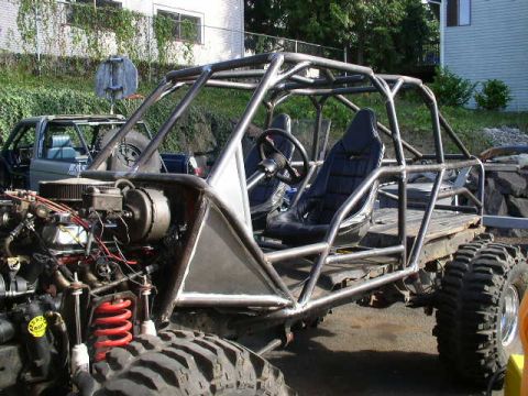 1979 Ford Bronco - A custom-built off-road buggy with a prominent roll cage and racing seats sits outdoors next to another vehicle.