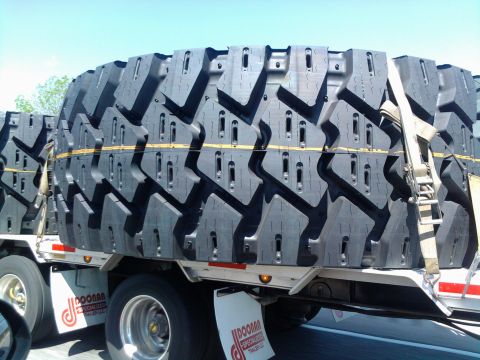 1989 Ford Bronco - Several large, heavy-duty tires are stacked and secured on a flatbed trailer under a clear sky.