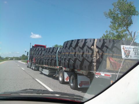 1989 Ford Bronco - A semi-truck transports a load of oversized tires down the road under a clear blue sky.