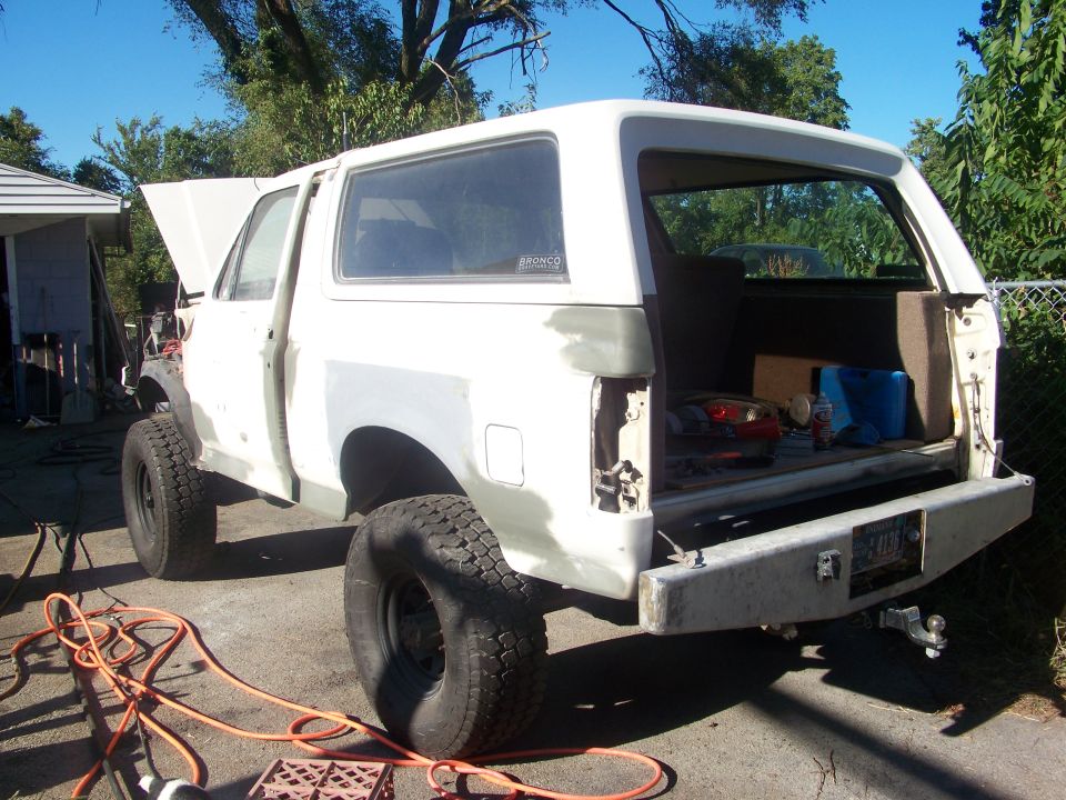 White SUV with hood open, bodywork in progress, rear bumper removed, spare tire visible