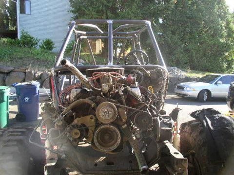 1979 Ford Bronco - Custom off-road buggy chassis with engine and roll cage visible. A sedan is parked nearby.